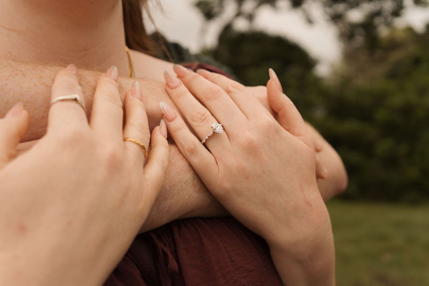 Close-up of two hands on a woman's chest, one wearing a diamond engagement ring during proposal photoshoot in sydney milk beach