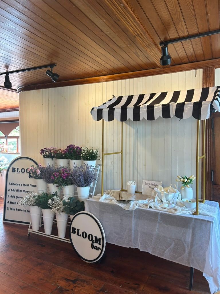 Bloom bar station with black and white striped awning, white flower buckets, and DIY floral arrangement display.