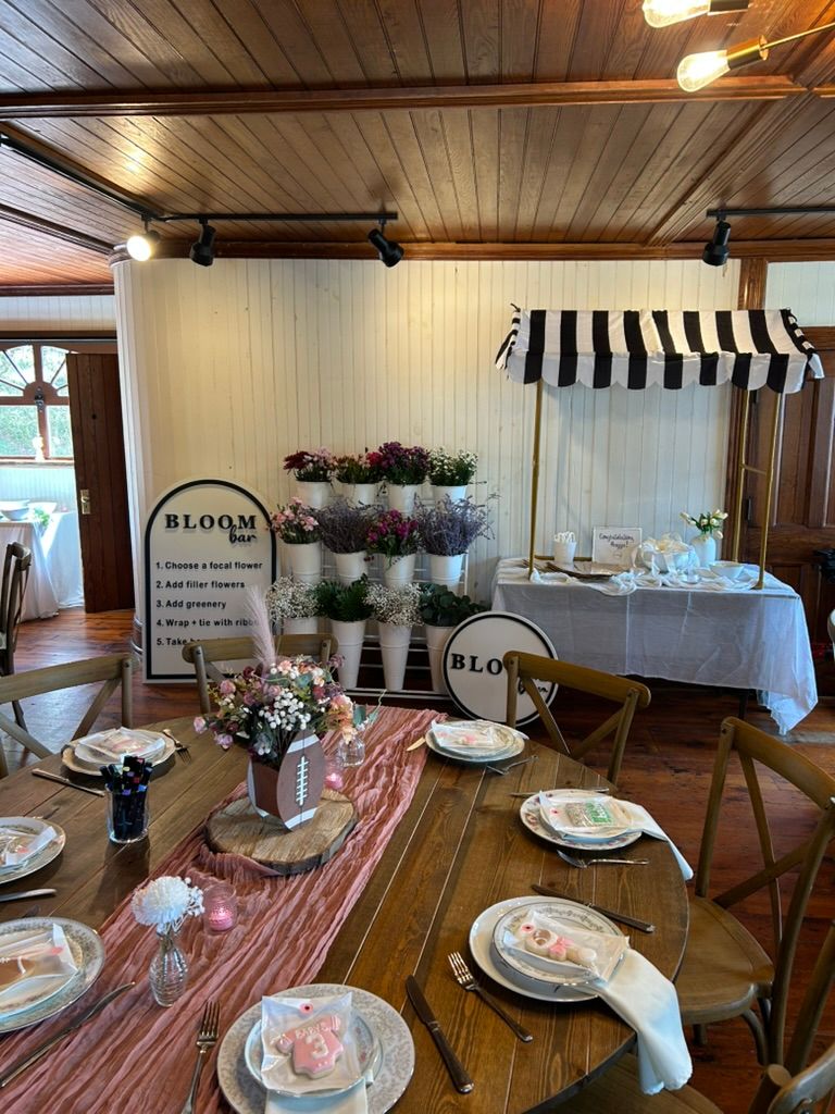 Indoor event space with bloom bar station, black striped awning, floral displays, and elegantly set dining tables.