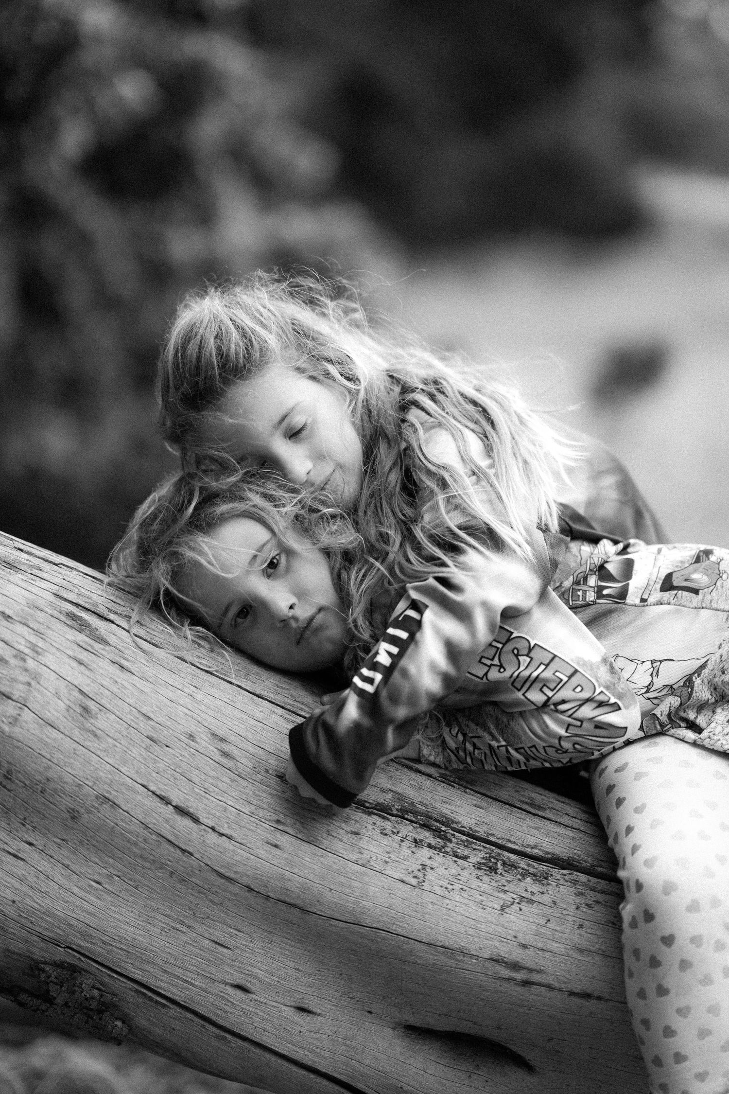 Children and adults sit on old tires under a large tree in a black and white outdoor photo.
