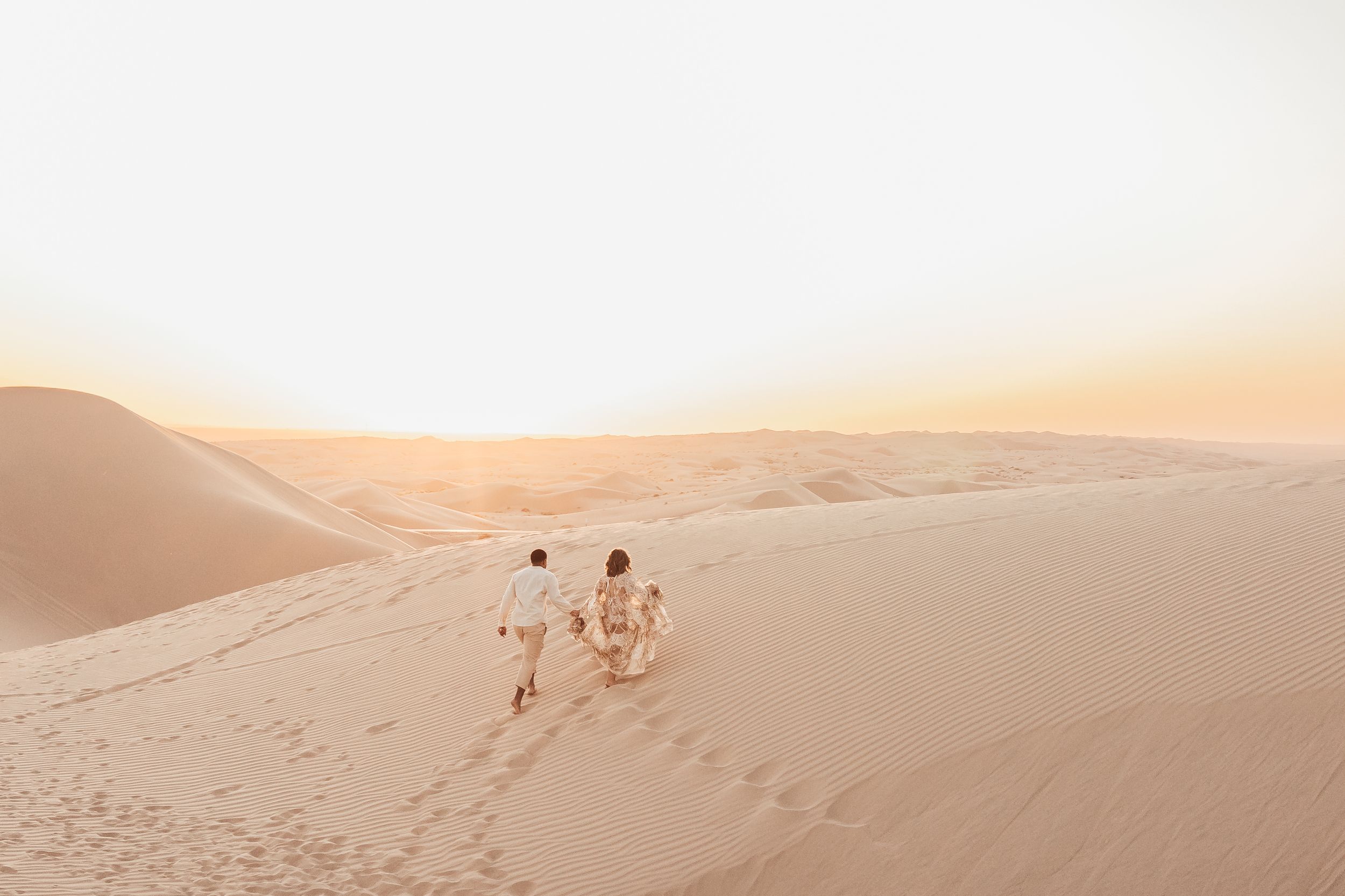 Family walking on golden sand dunes at sunset in a vast desert landscape, leaving footprints behind.