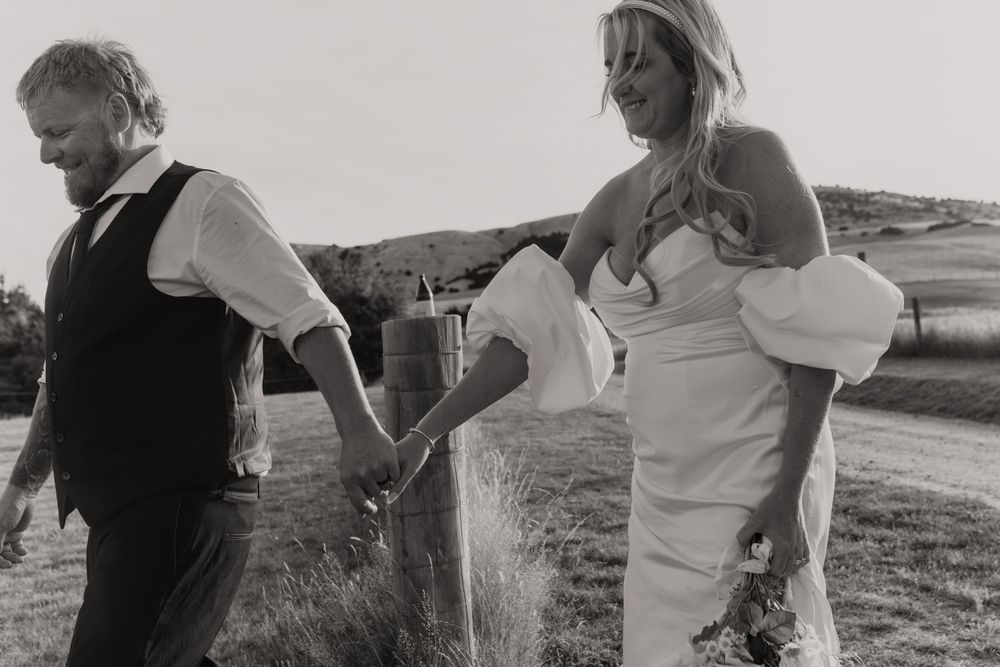 Black and white photo of a bride and groom holding hands walking outdoors on their wedding day.