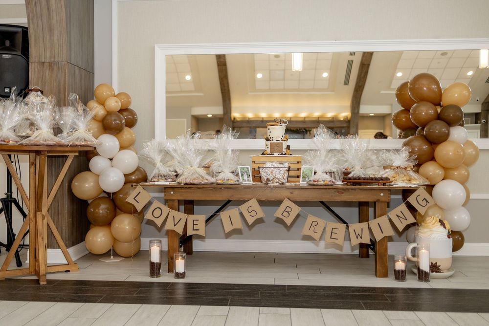 Rustic bridal shower dessert table with brown and white balloon arch, burlap banner reading Love Is Brewing.