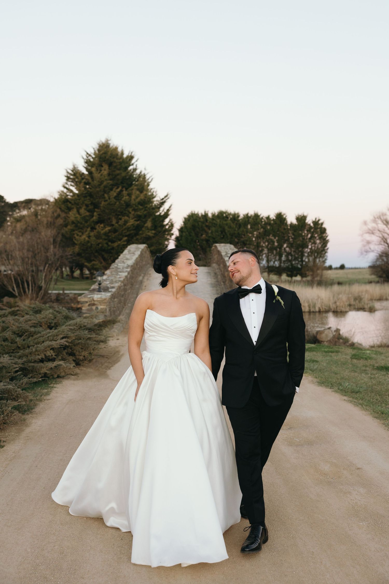 Bride and groom sitting on green grass, sharing a romantic moment, bride in white strapless gown, groom in black suit.