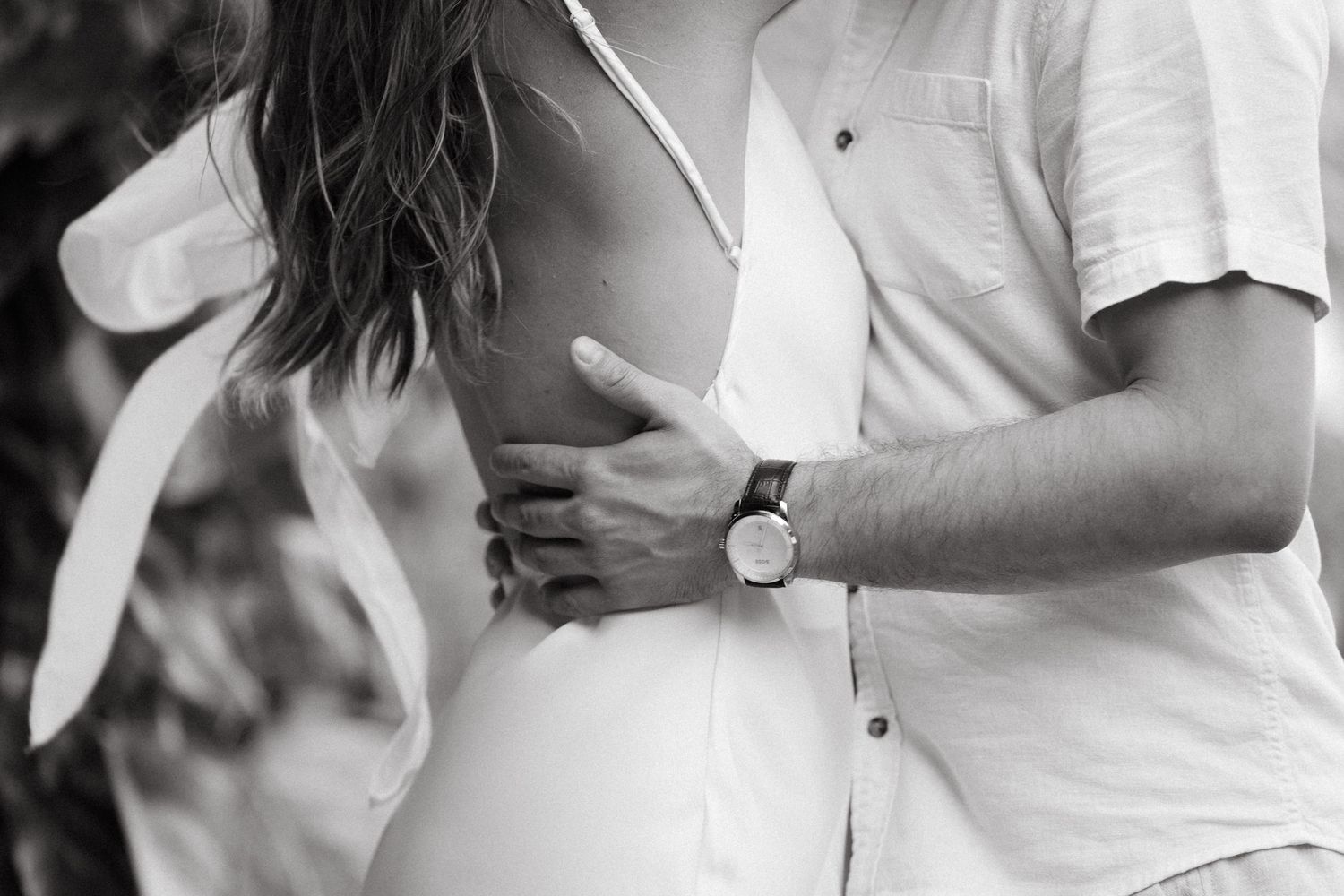Black and white close-up of a couple embracing, showing a mans hand with a watch around a womans waist.