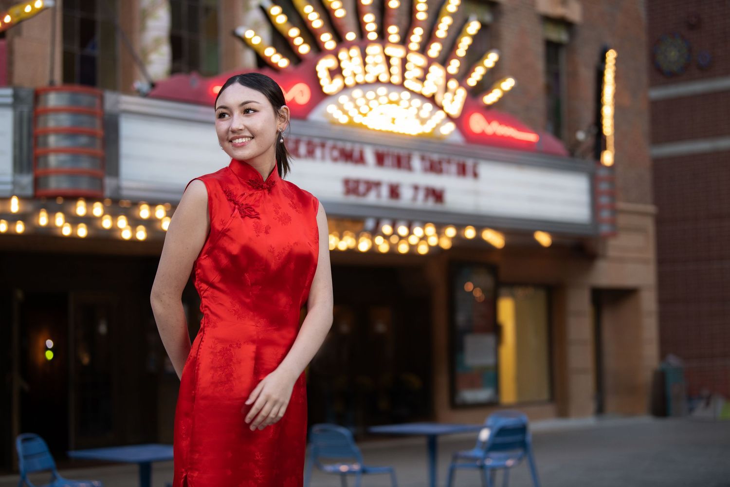Woman in red cheongsam dress posing outside Chateau theater with neon marquee lights at night.