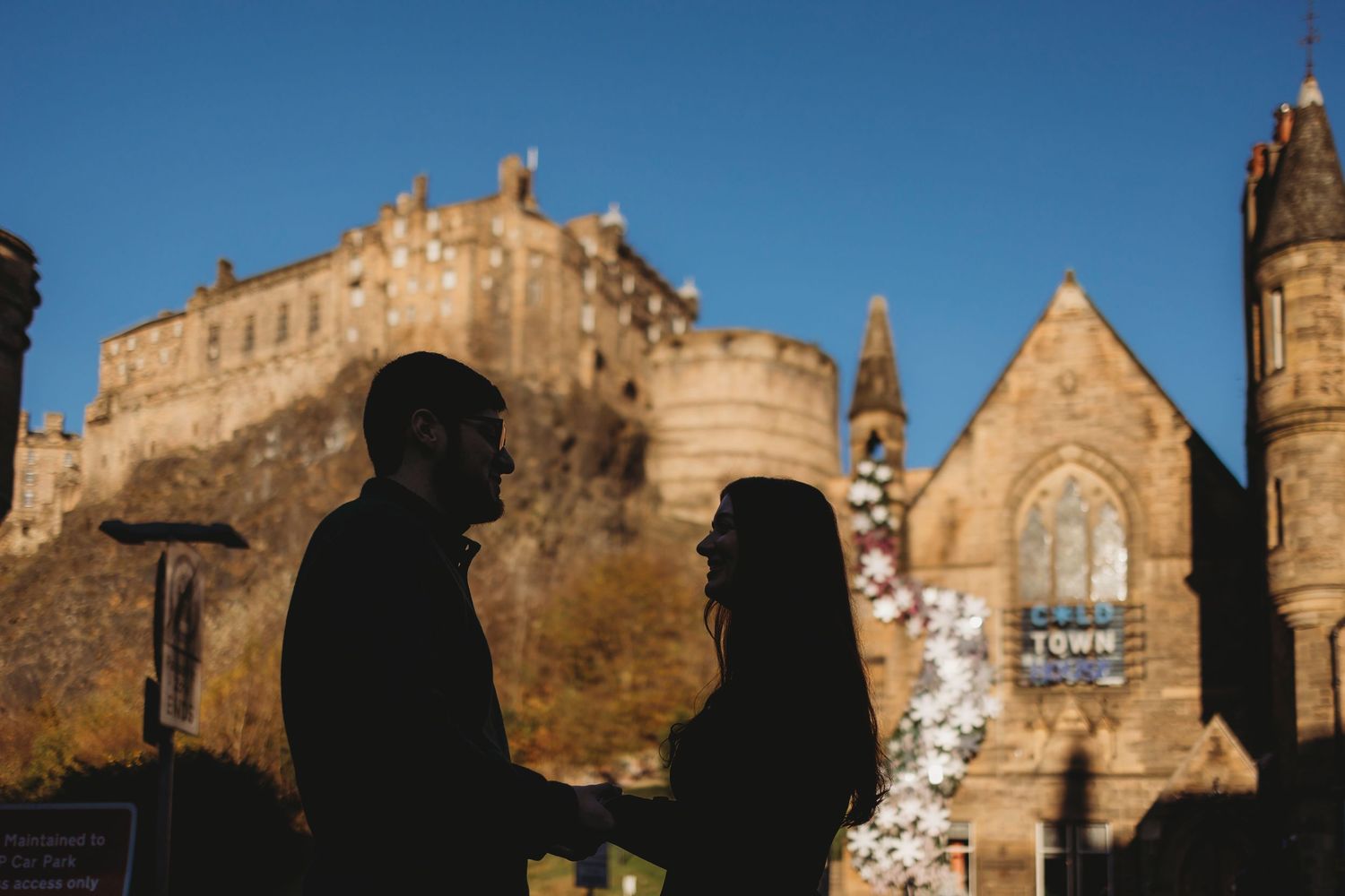 Four people smiling and chatting outdoors near Edinburgh Castle on a rocky hill in Scotland.