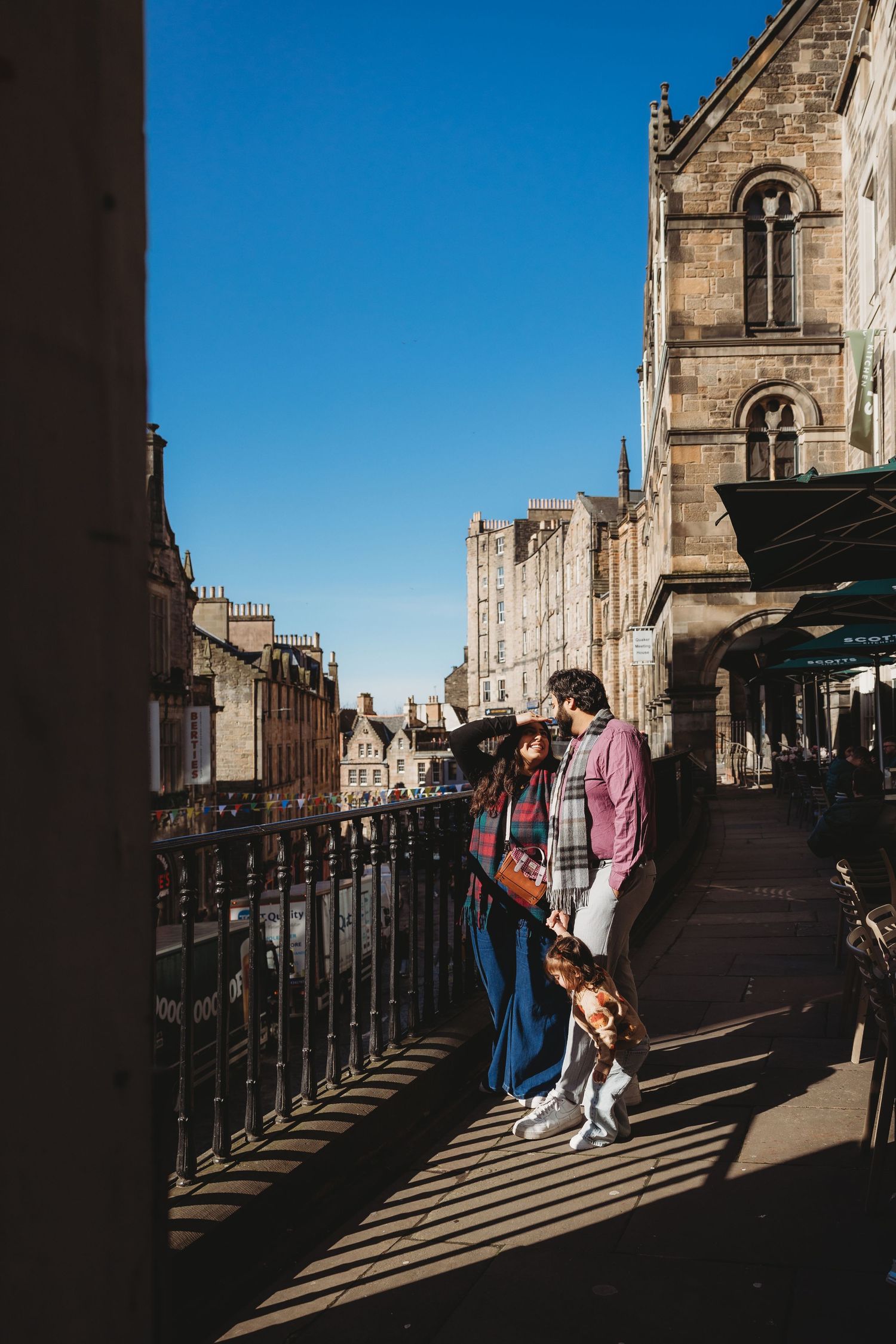 A couple with a child walks along a sunny cobblestone street in Edinburgh, Scotland.