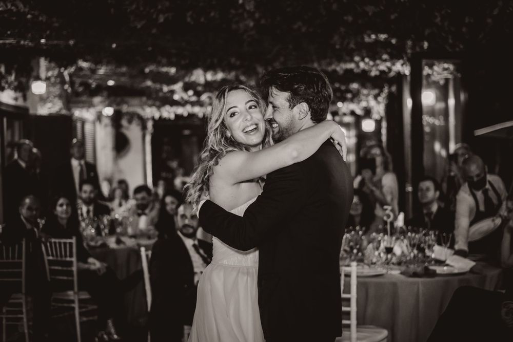 A romantic first dance moment at a wedding reception with string lights and tables in the background.