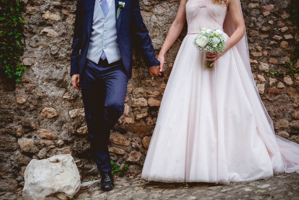 Couple poses for wedding photos against rustic stone wall backdrop.