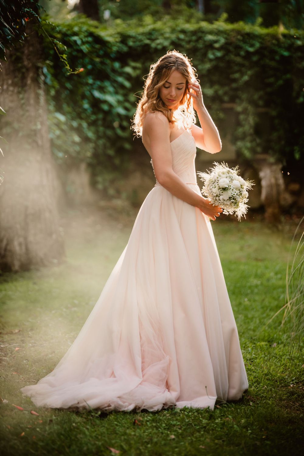 Ethereal bridal portraits in a blush gown amid misty garden scenery.