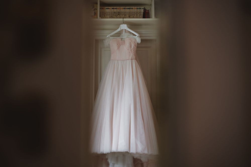 White wedding dress hangs elegantly against dark background in preparation for the ceremony.