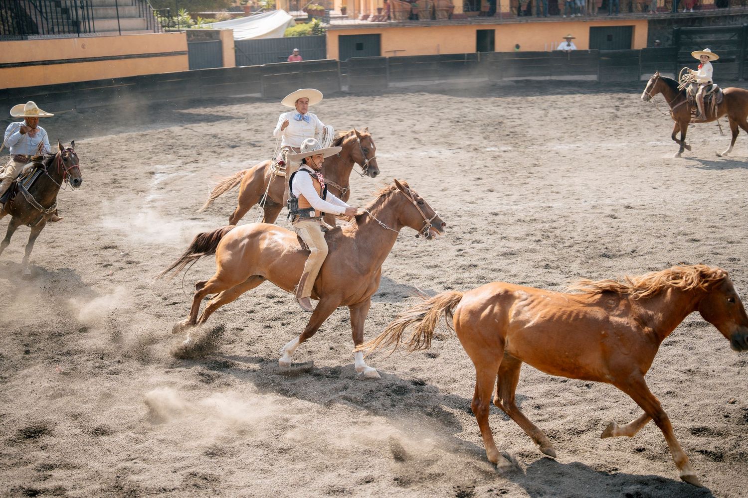 Mexican charreada equestrian show with riders in traditional costumes performing in a sandy arena.
