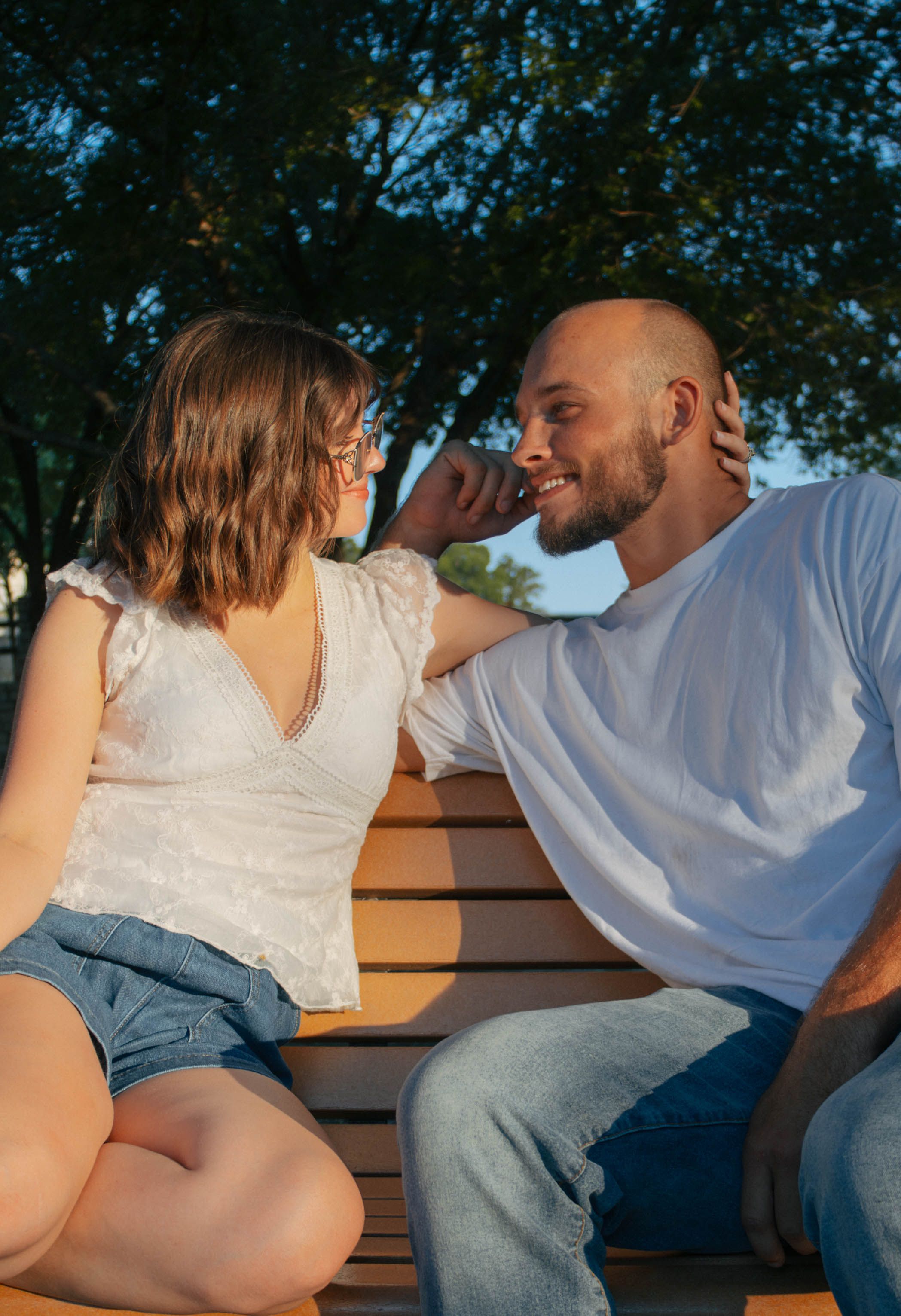 Couple sitting on a bench outdoors smiling at each other in warm golden hour sunlight.