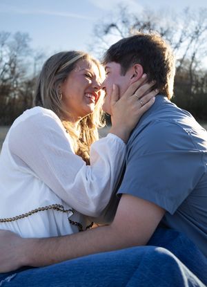 A smiling couple shares a romantic moment outdoors, with the woman touching the man's face against a blue sky.