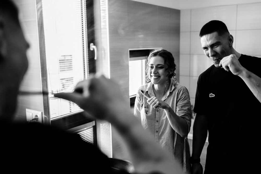 Black and white photo of a bride and groom brushing teeth together in a bathroom before their wedding.