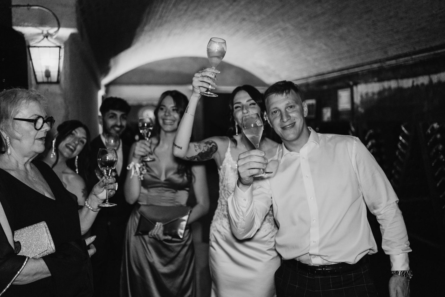 Joyful wedding guests celebrating and toasting with champagne glasses in black and white photo.