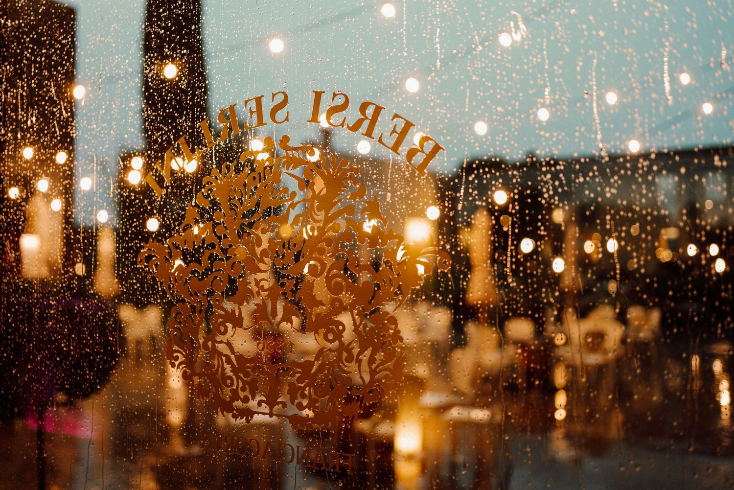 Romantic rainy wedding venue window with glowing candles and decorative gold lettering reflection.