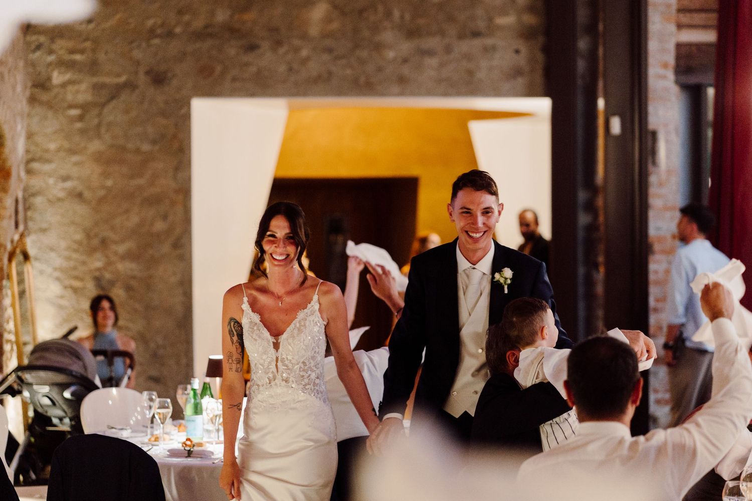Smiling bride and groom making grand entrance into rustic stone wedding reception hall.