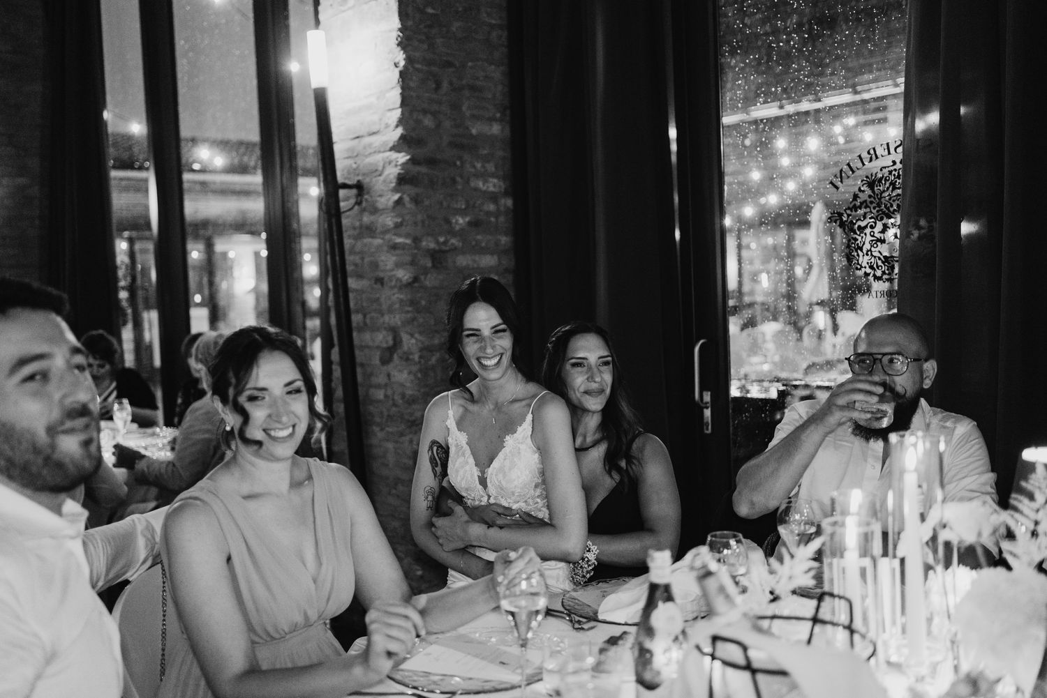 Wedding guests laugh and smile joyfully together at a beautifully decorated reception dinner table with candles and flowers.