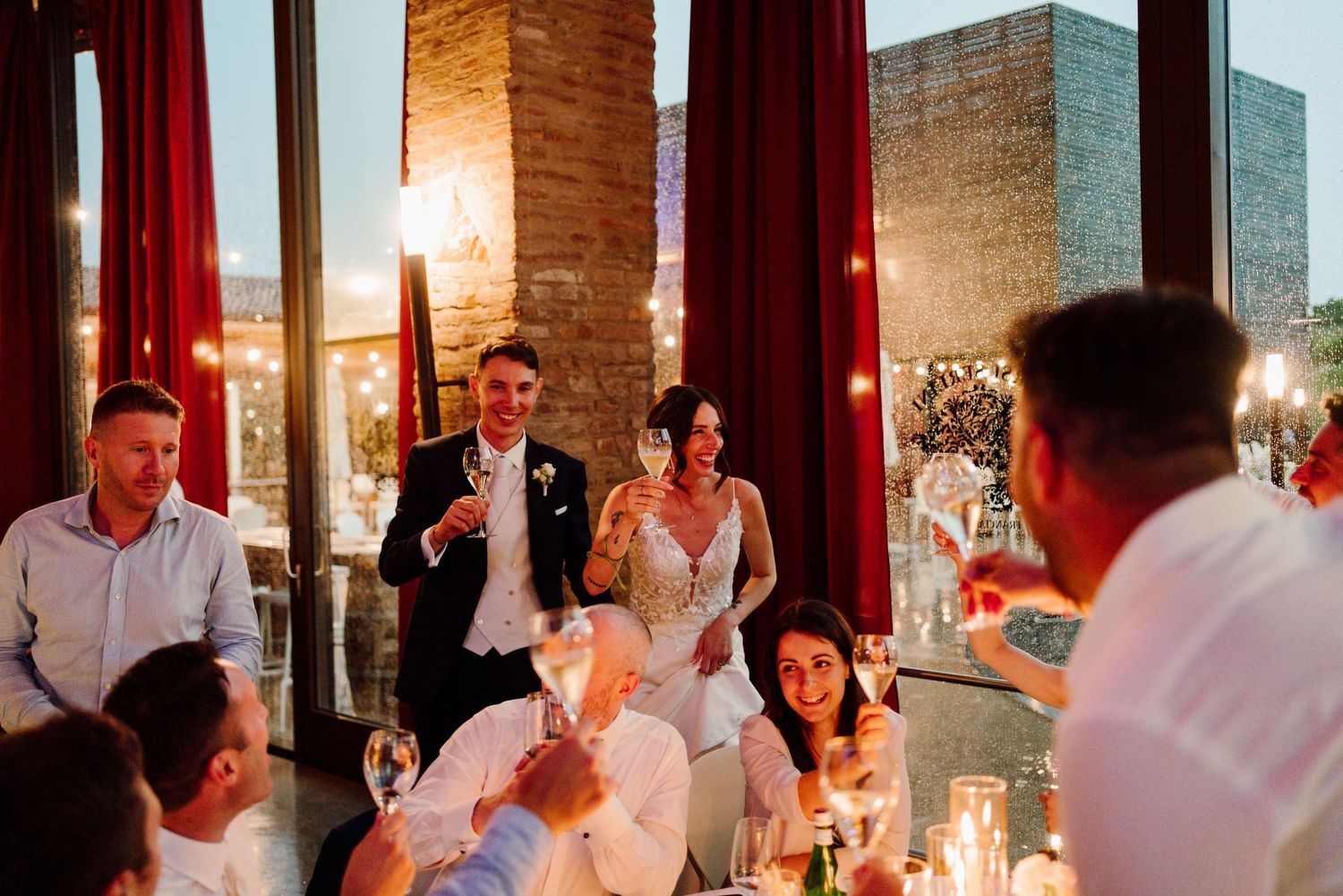 Bride and groom share a champagne toast with smiling guests at their elegant candlelit wedding reception venue.