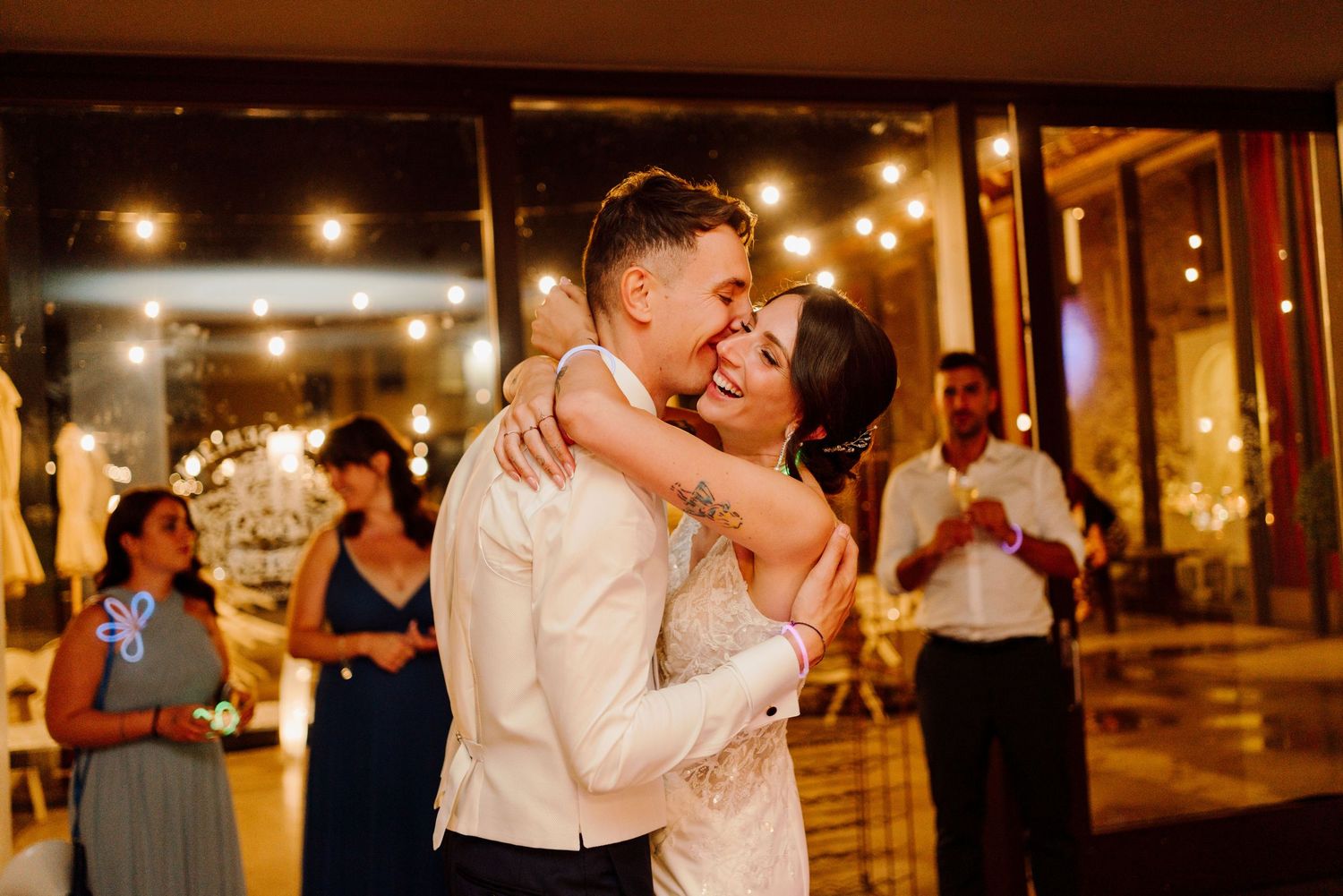 Bride and groom share a joyful first dance embrace surrounded by warm string lights at wedding reception.