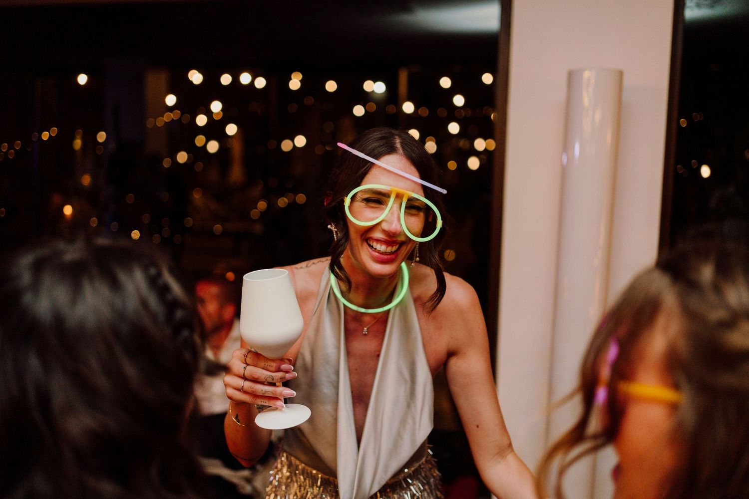 Wedding guest wearing oversized novelty glasses smiles while holding a drink at a festive reception.