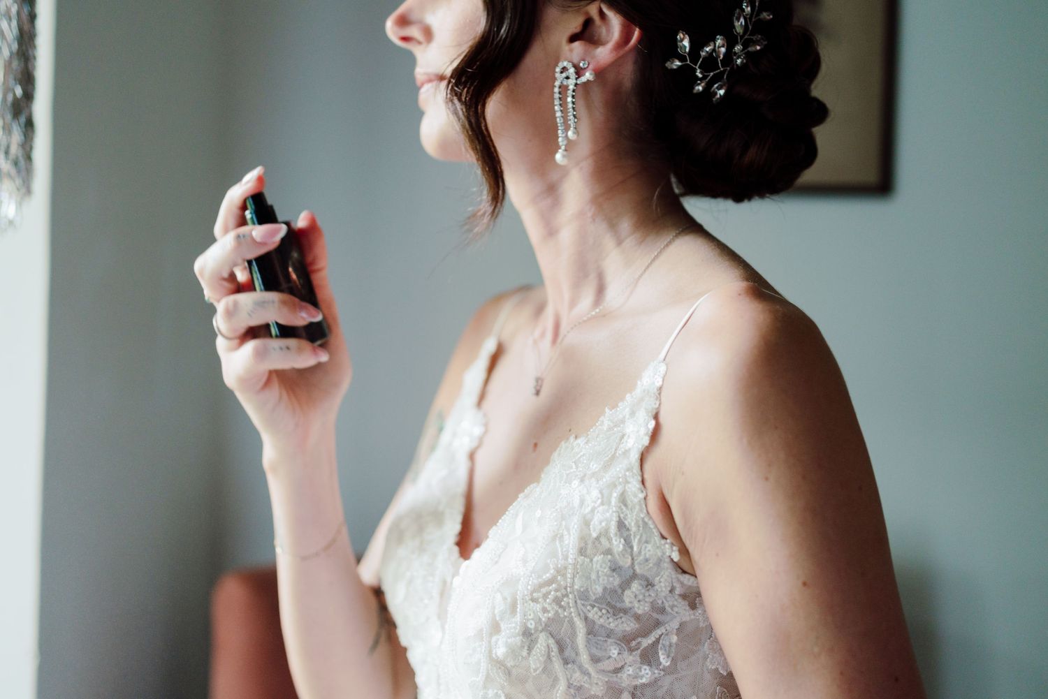 Elegant bride in lace wedding dress spraying perfume on her neck before the wedding ceremony.