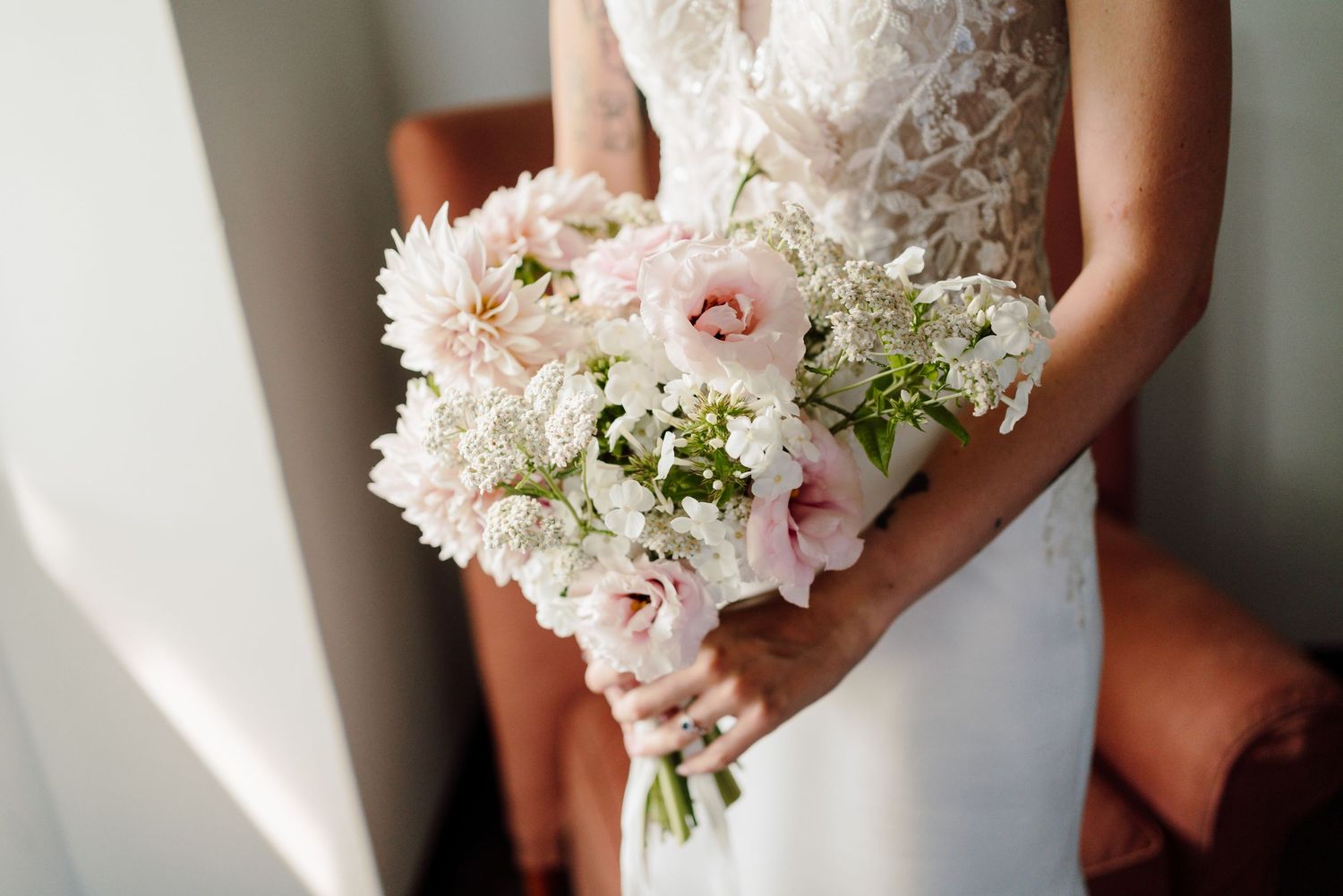Close-up of bride holding a delicate bouquet of soft pink roses and white flowers on wedding day.