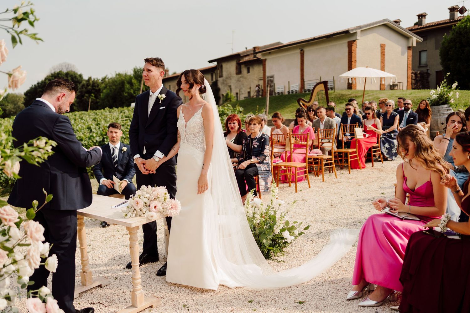 Bride and groom stand at altar during outdoor vineyard wedding ceremony with seated guests watching.