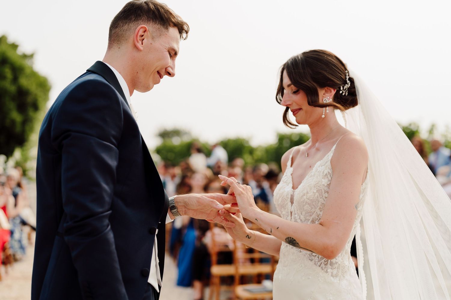 Bride and groom exchanging rings during outdoor wedding ceremony, smiling joyfully.