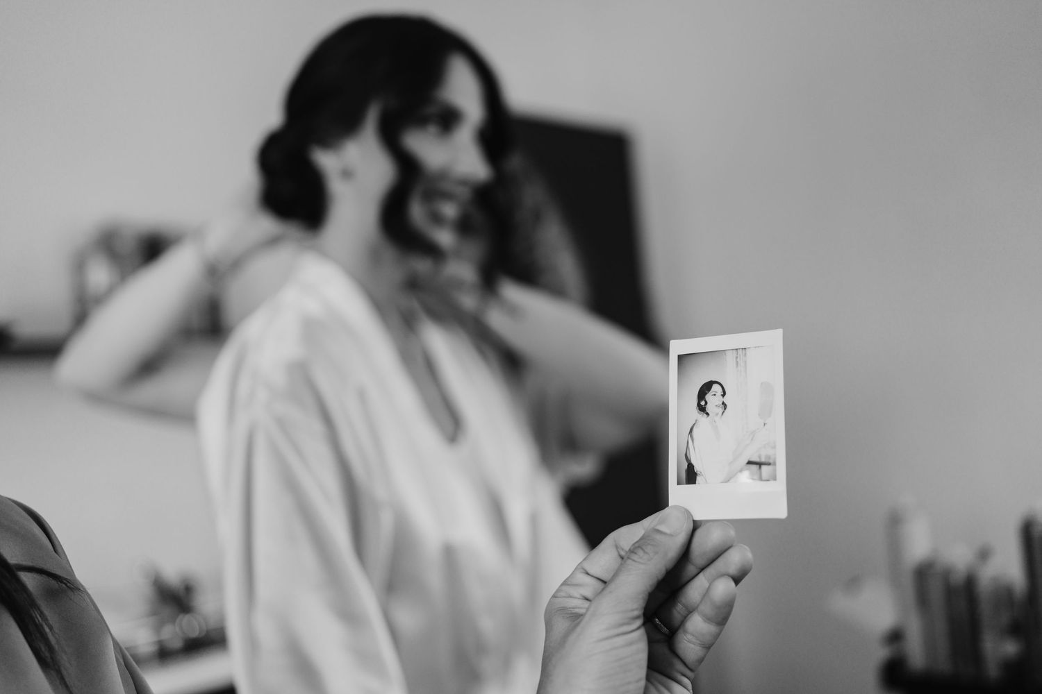 Creative black and white shot of Polaroid photo held up showing bride getting ready in the background.