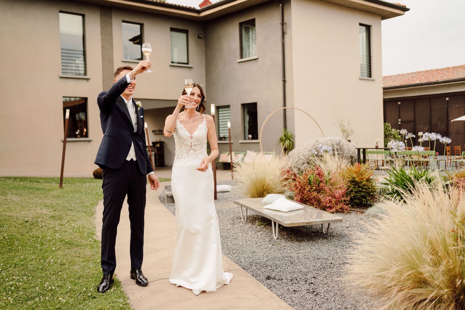 Bride and groom laughing outdoors at a winery venue, with the bride in a sleek white gown and groom in a navy suit.