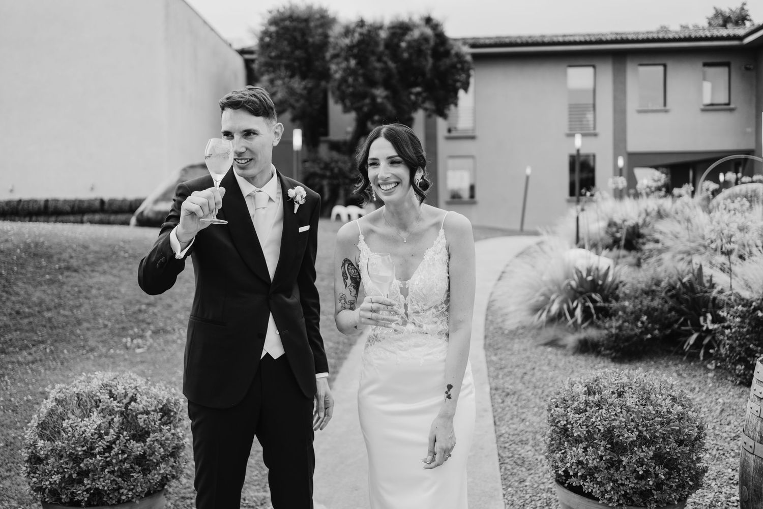 Black and white photo of a smiling bride and groom walking together outside a wedding venue.