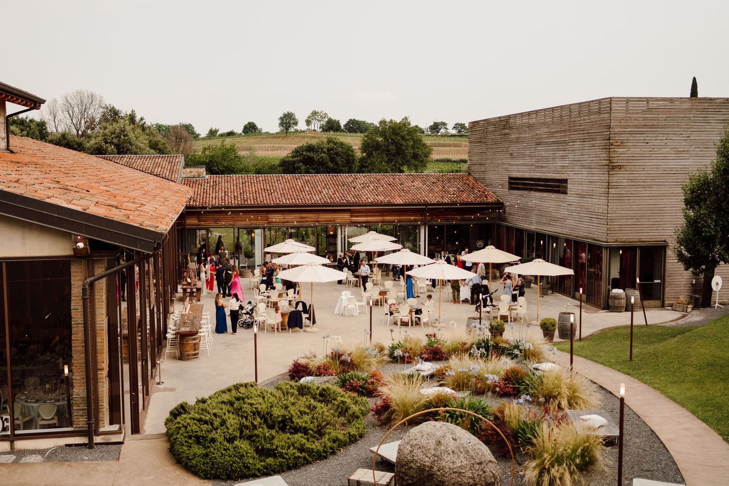 Aerial view of an elegant winery wedding venue with guests mingling under white umbrellas on a patio.