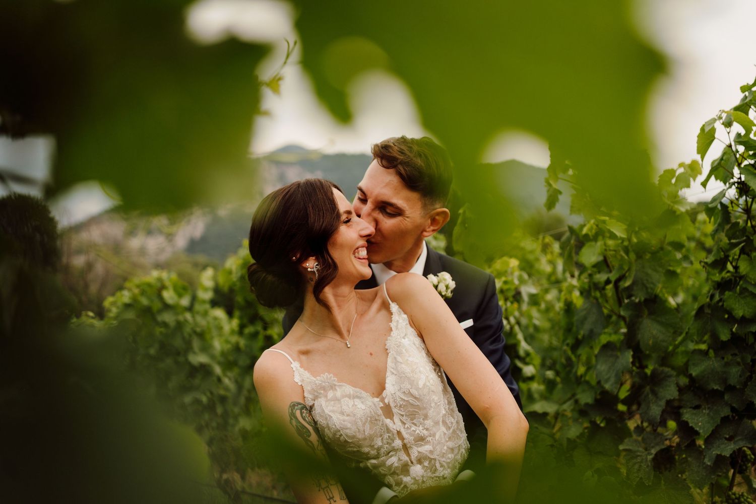 Bride and groom share an intimate moment framed by lush green vineyard leaves.