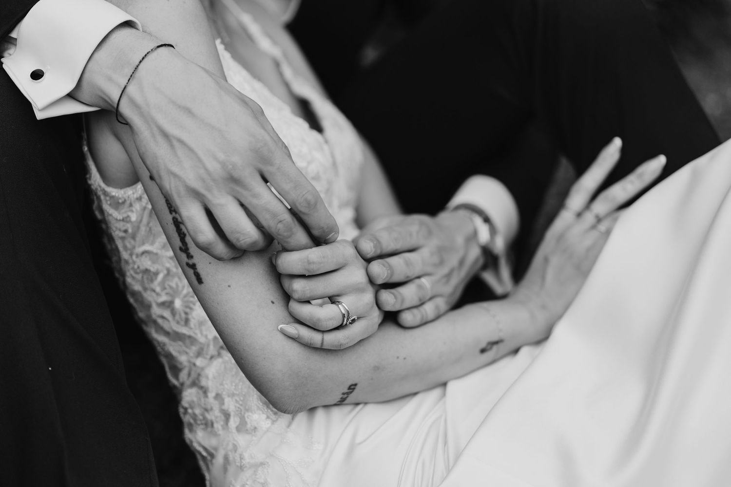 Black and white close-up of bride and groom's hands with wedding rings entwined.