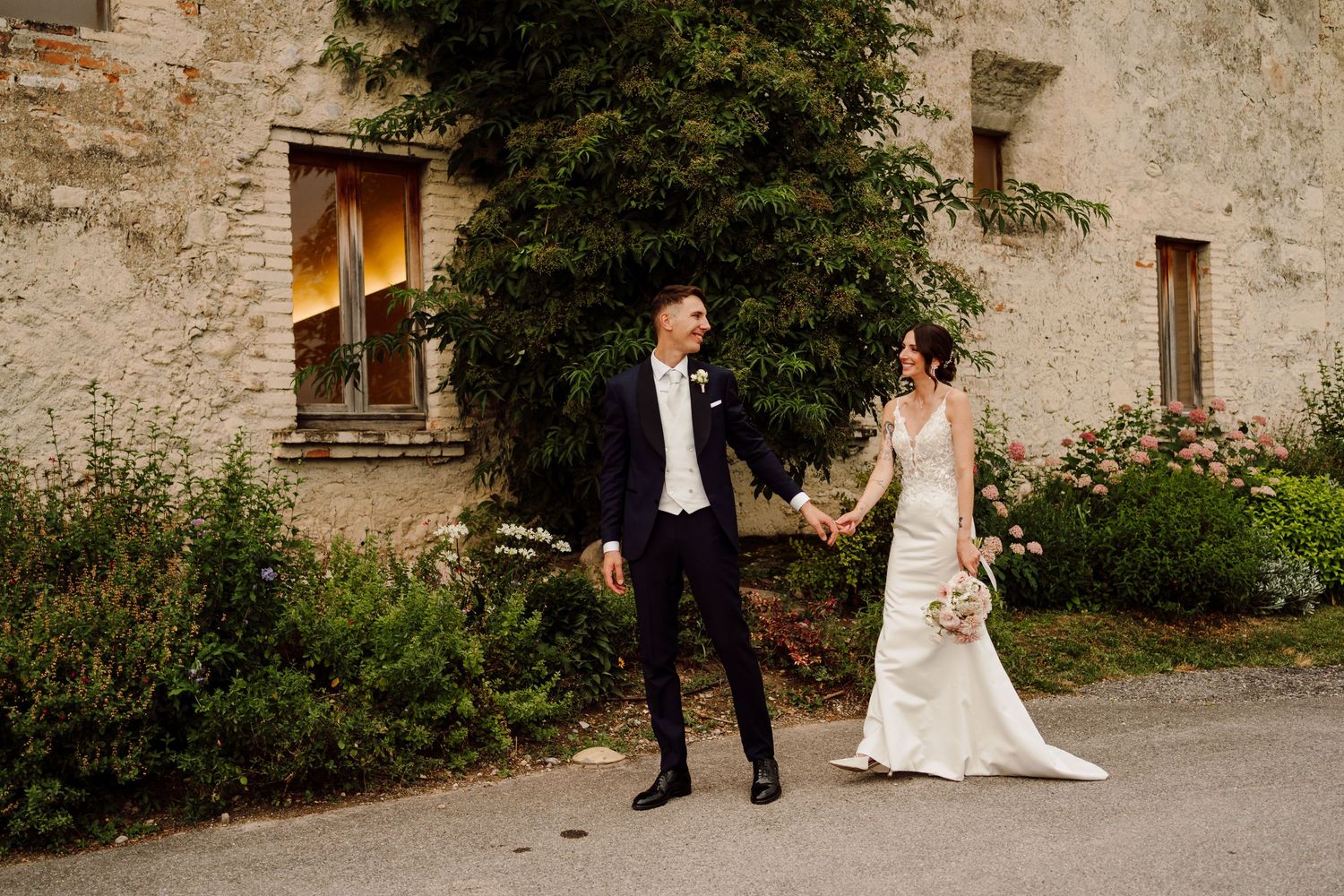 Bride and groom walk hand in hand past a charming rustic stone venue.