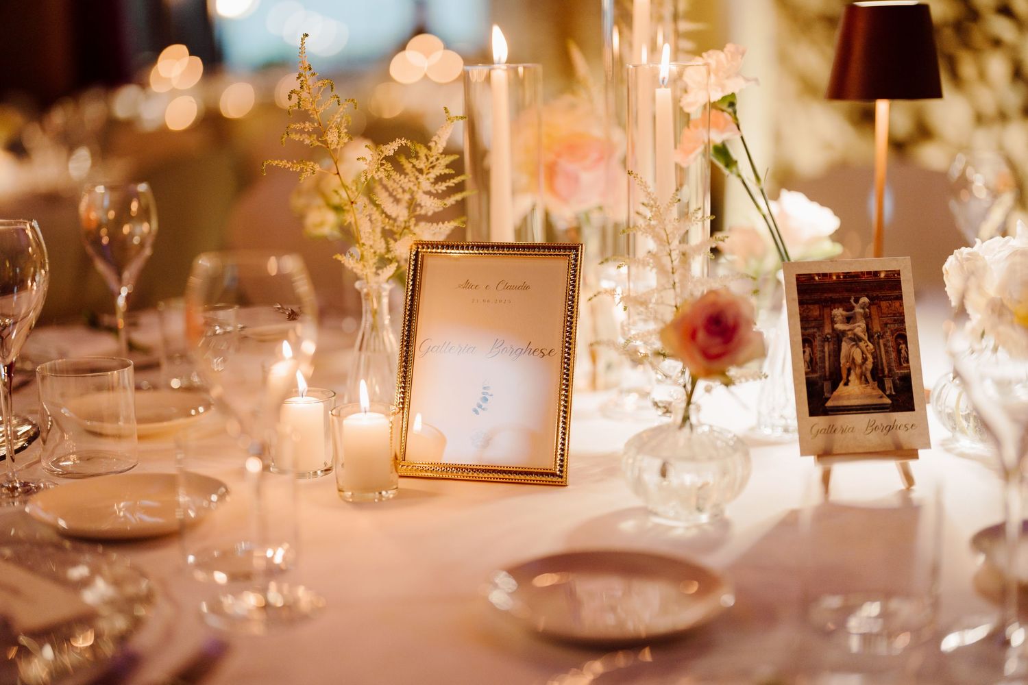 Elegant wedding reception table with gold-framed number, candles, pink flowers, and crystal glassware.