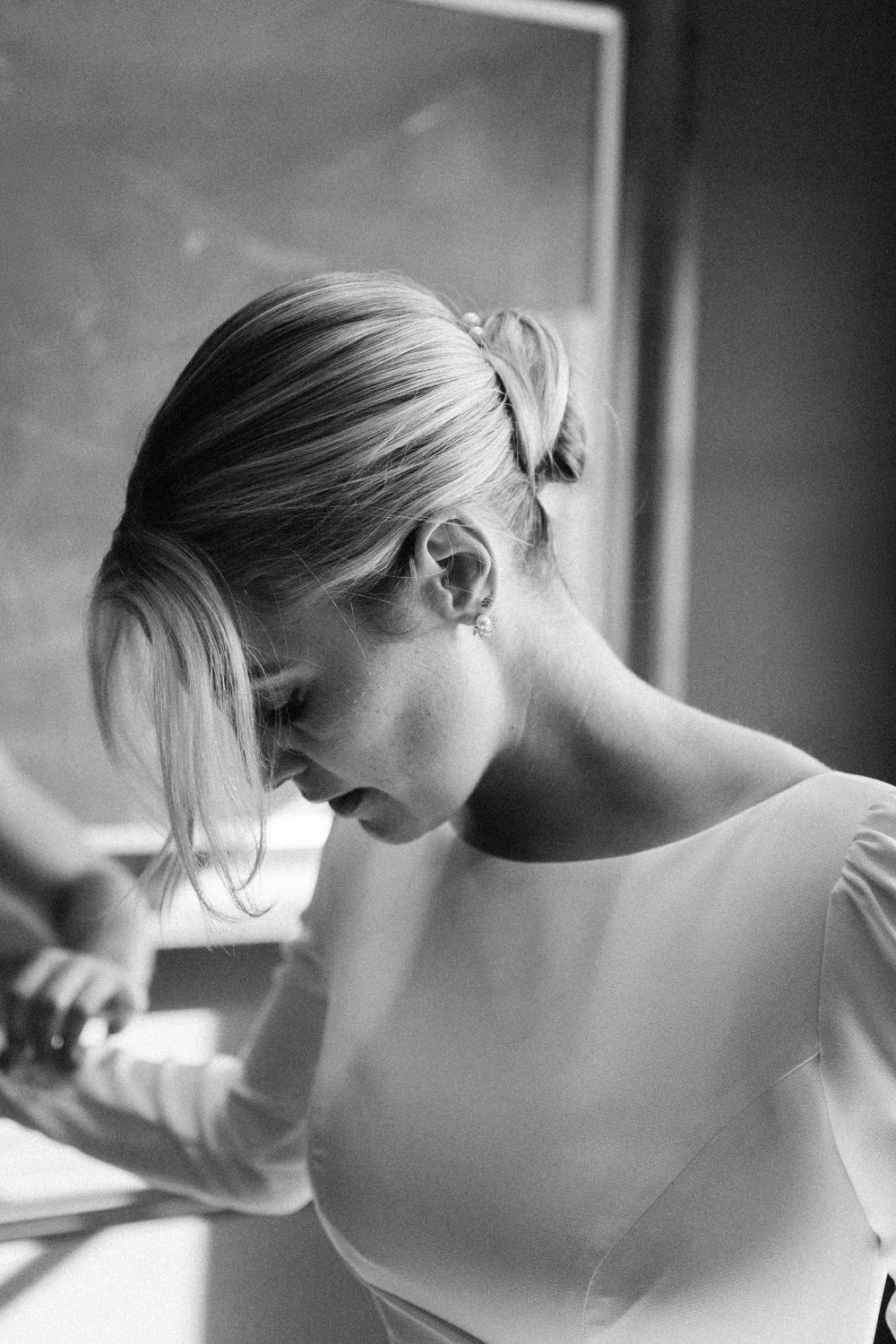 Black and white portrait of bride with updo hairstyle in wedding dress near window.