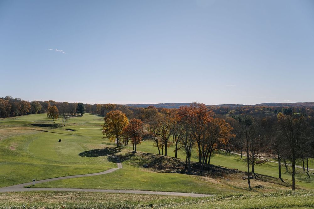 Scenic autumn golf course landscape with colorful fall foliage under clear blue sky.