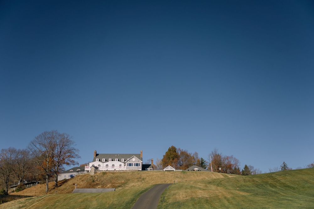 White farmhouse on a green hillside under a clear blue sky with a winding driveway.