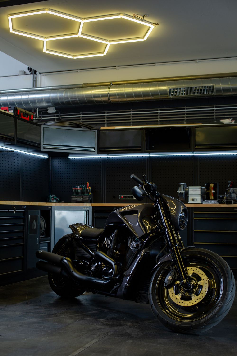 Custom black and gold motorcycle displayed in a modern dark garage with hexagonal LED lighting.
