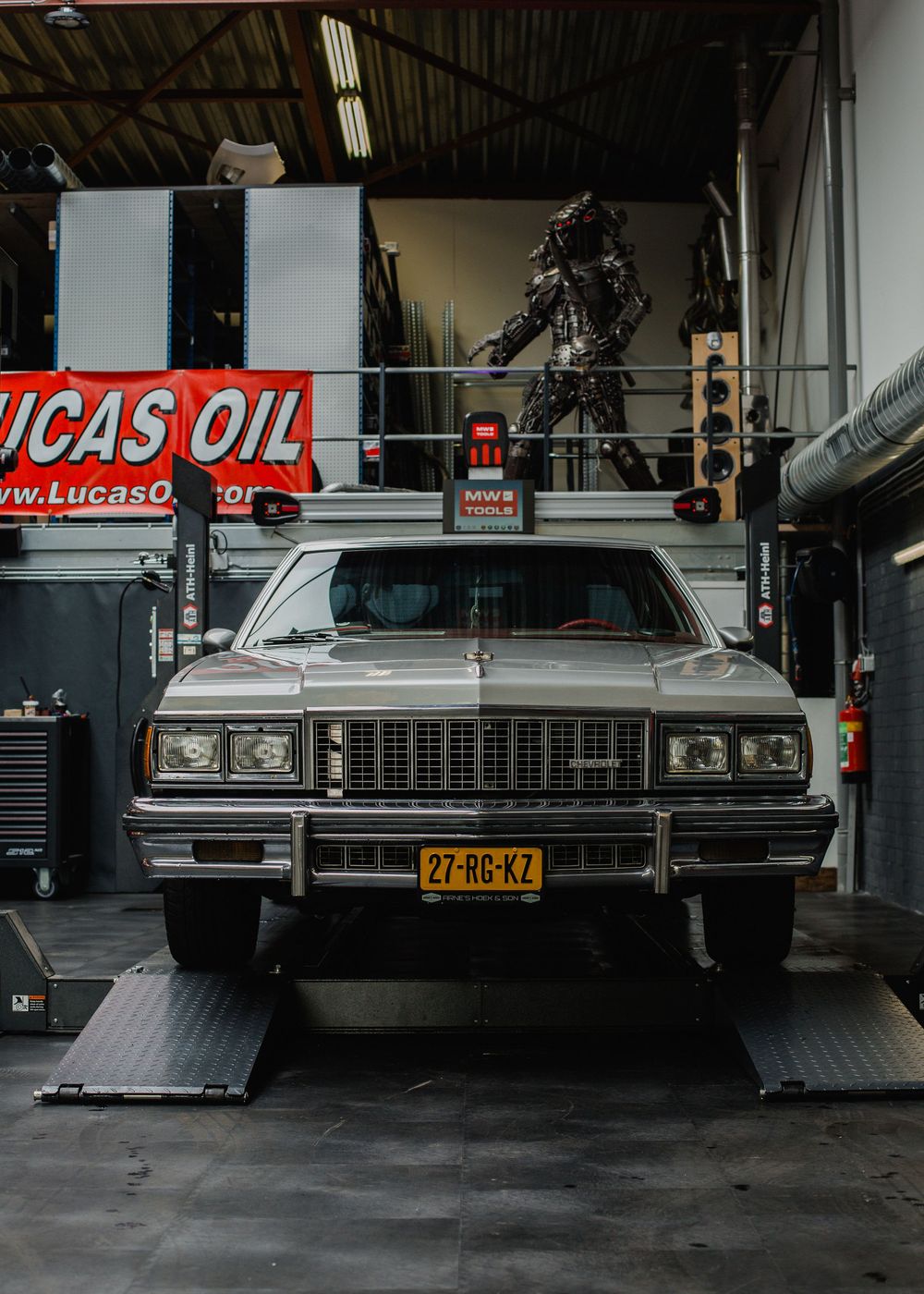 Vintage silver American classic car with Dutch license plate parked inside a Lucas Oil garage.