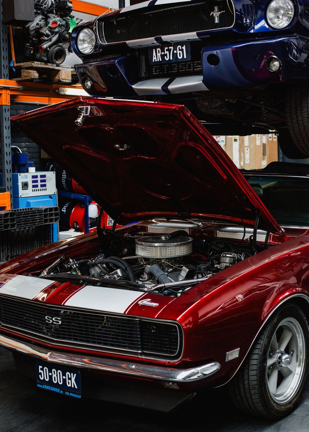 Restored red Chevrolet Camaro SS muscle car with open hood showing chrome engine in a garage.