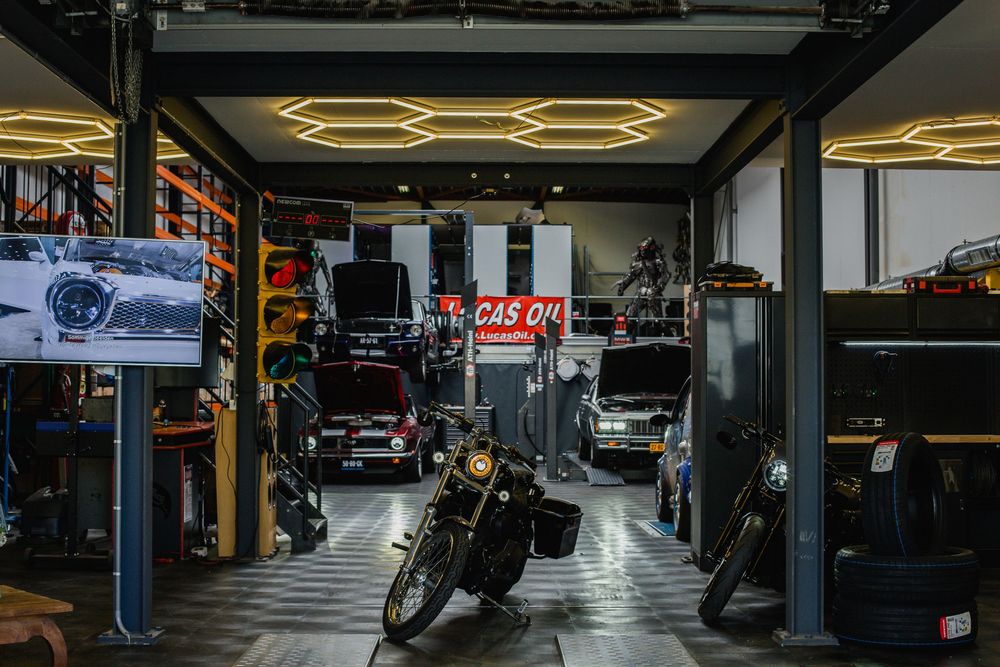 Interior view of a classic car garage workshop with motorcycles and vehicles under hexagonal lights.