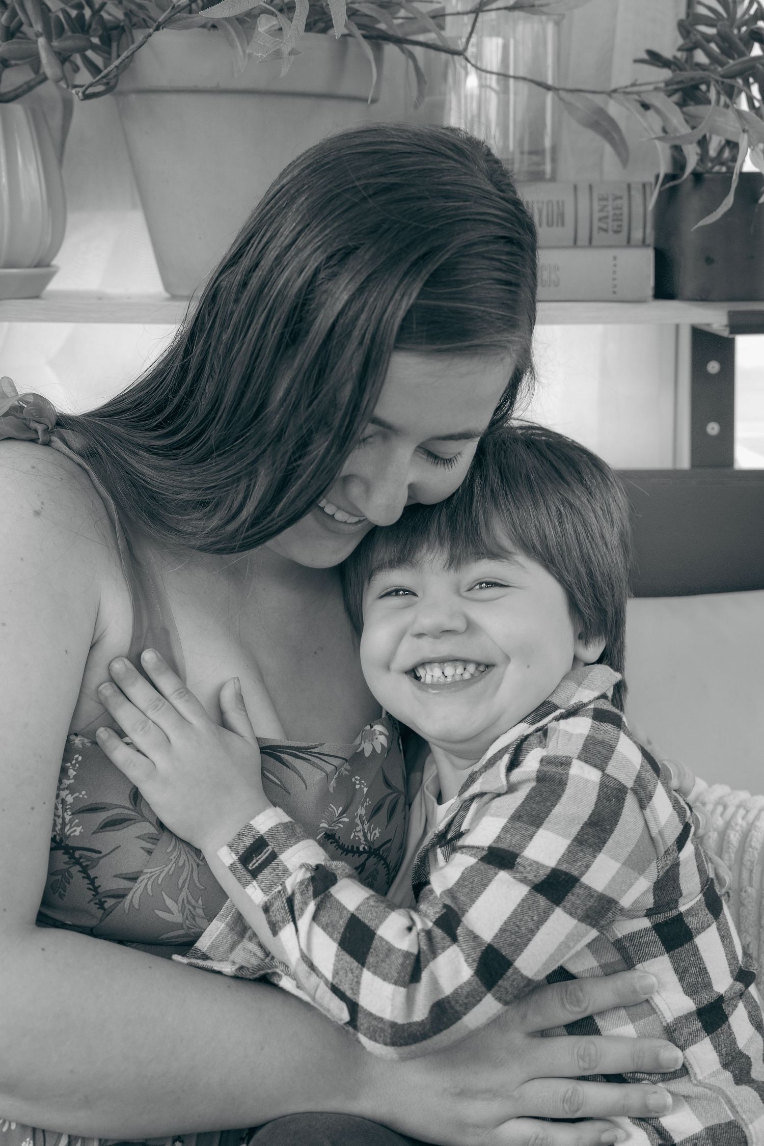 Black and white photo of a smiling boy hugging a woman, sharing a joyful moment together indoors.