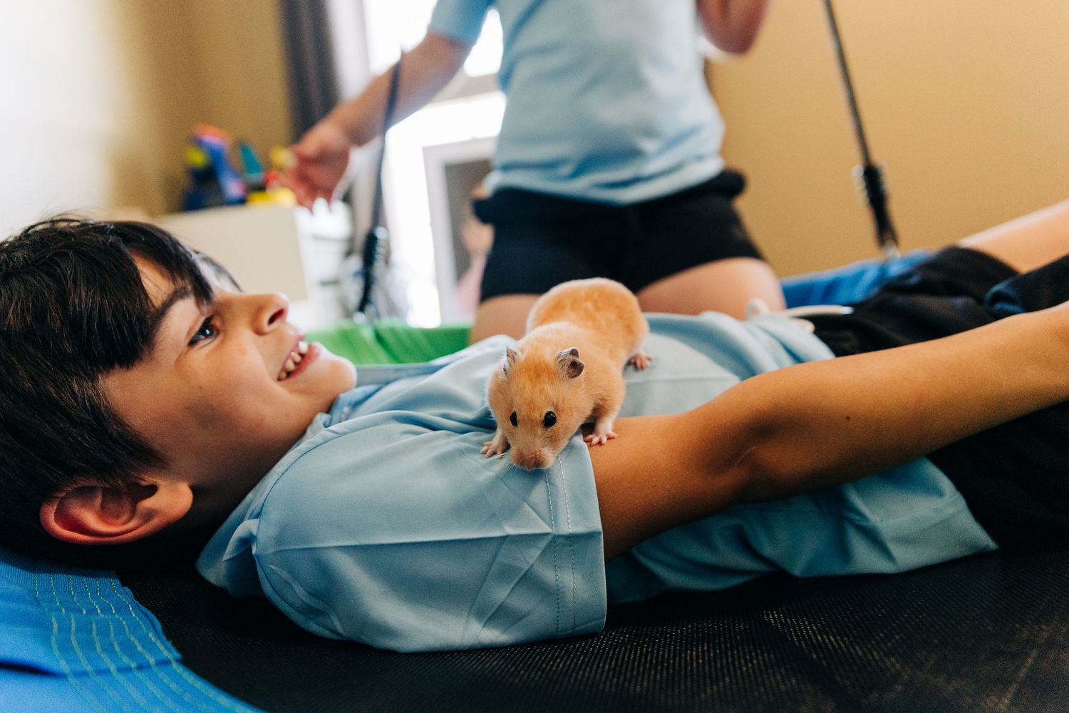 Boy lying down smiling while a hamster walks on his chest during a fun pet interaction activity.