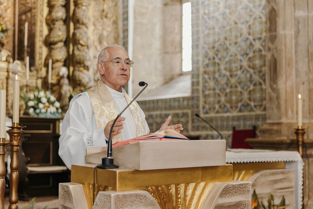 A priest in white vestments delivers a sermon at a pulpit in an ornate church.Jo Matos Fotografia Reportagem de Batismo