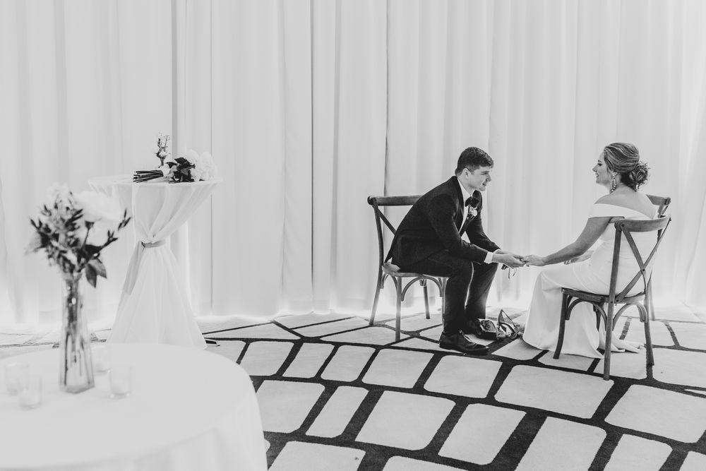 Black and white photo of bride and groom sitting in chairs holding hands during wedding ceremony.